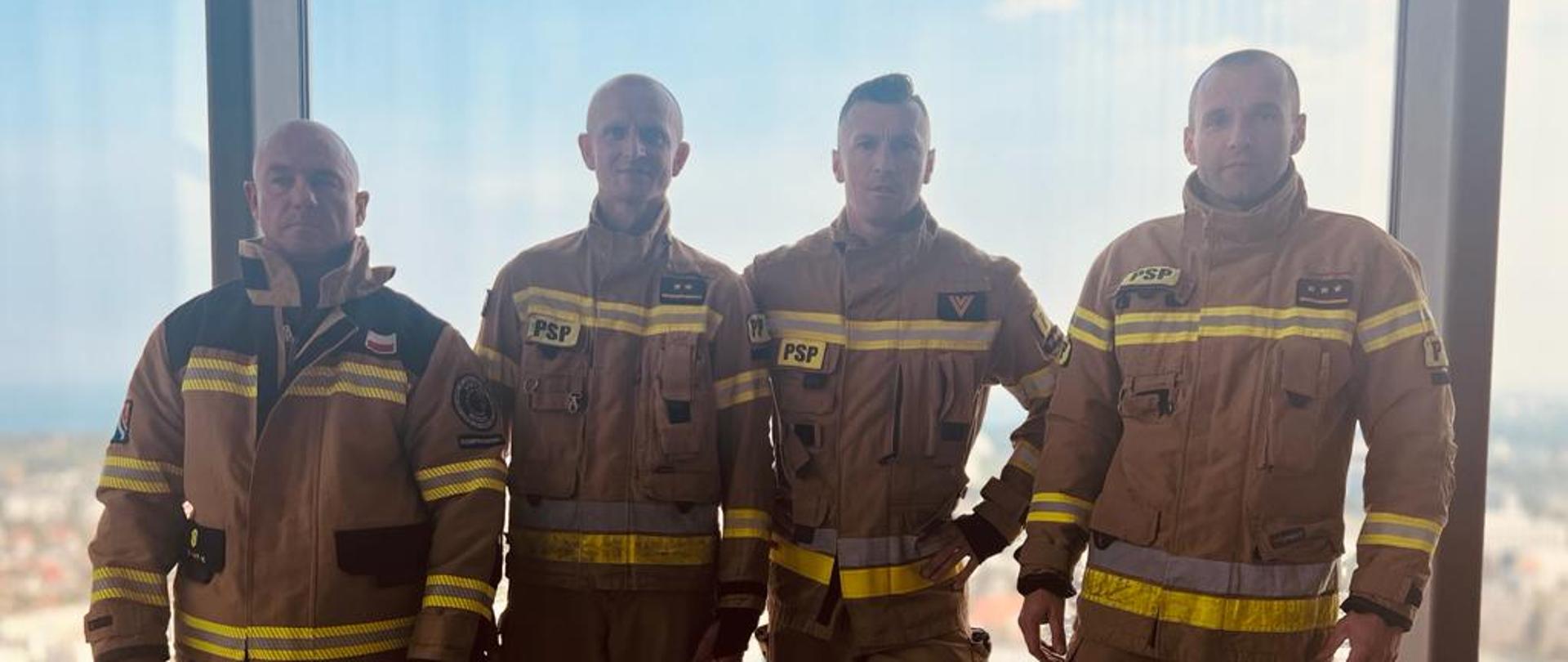 Zdjęcie przedstawia czterech strażaków w umundurowaniu piaskowym. 