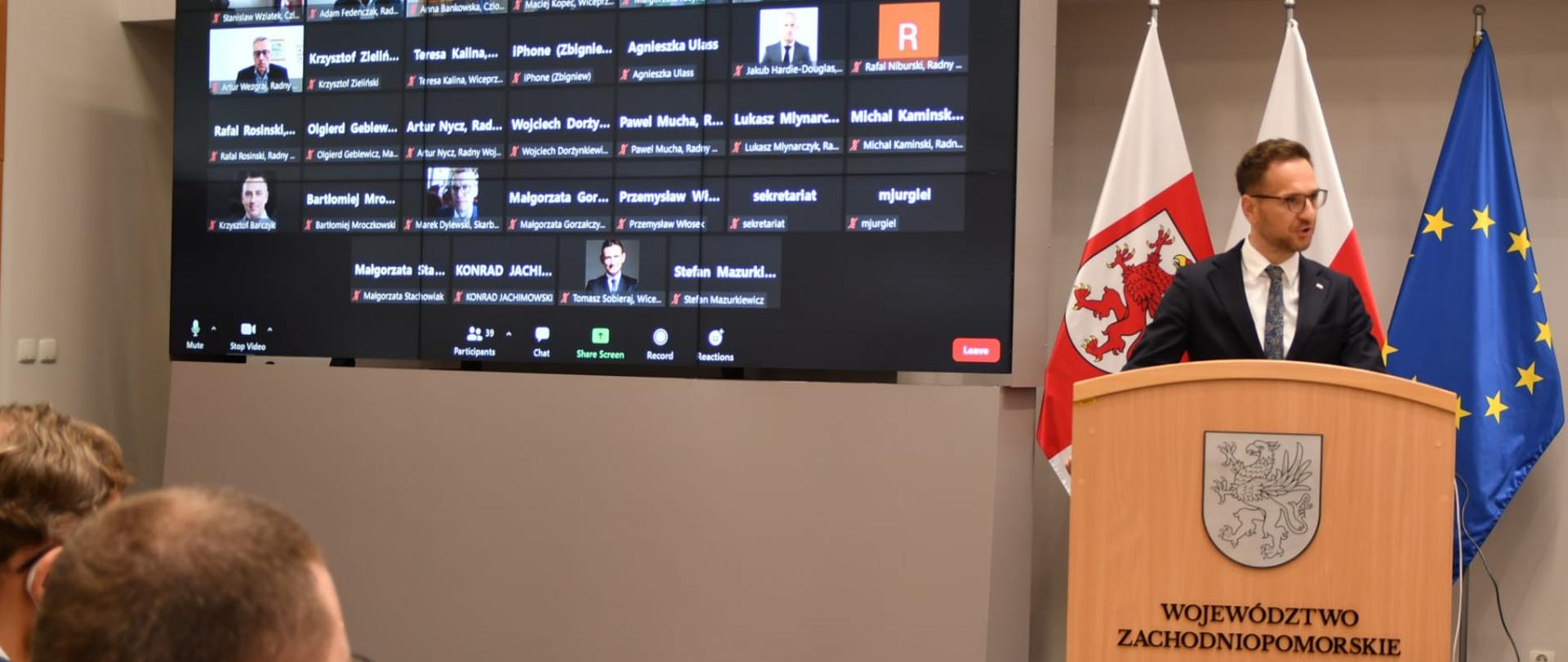 wiceminister Waldemar Buda mówi z mównicy, na której umieszczony jest herb województwa zachodniopomorskiego