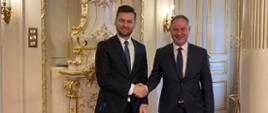 Na zdjęciu minister sportu i turystyki Kamil Bortniczuk i czeski minister do spraw sportu Peter Gazdik. Ministrowie ściskają sobie dłoń. Minister Kamil Bortniczuk przebywał z wizytą w Pradze
