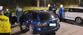 Funkcjonariusze i kontrolowani kierowcy obok dwóch pojazdów taxi na parkingu 
