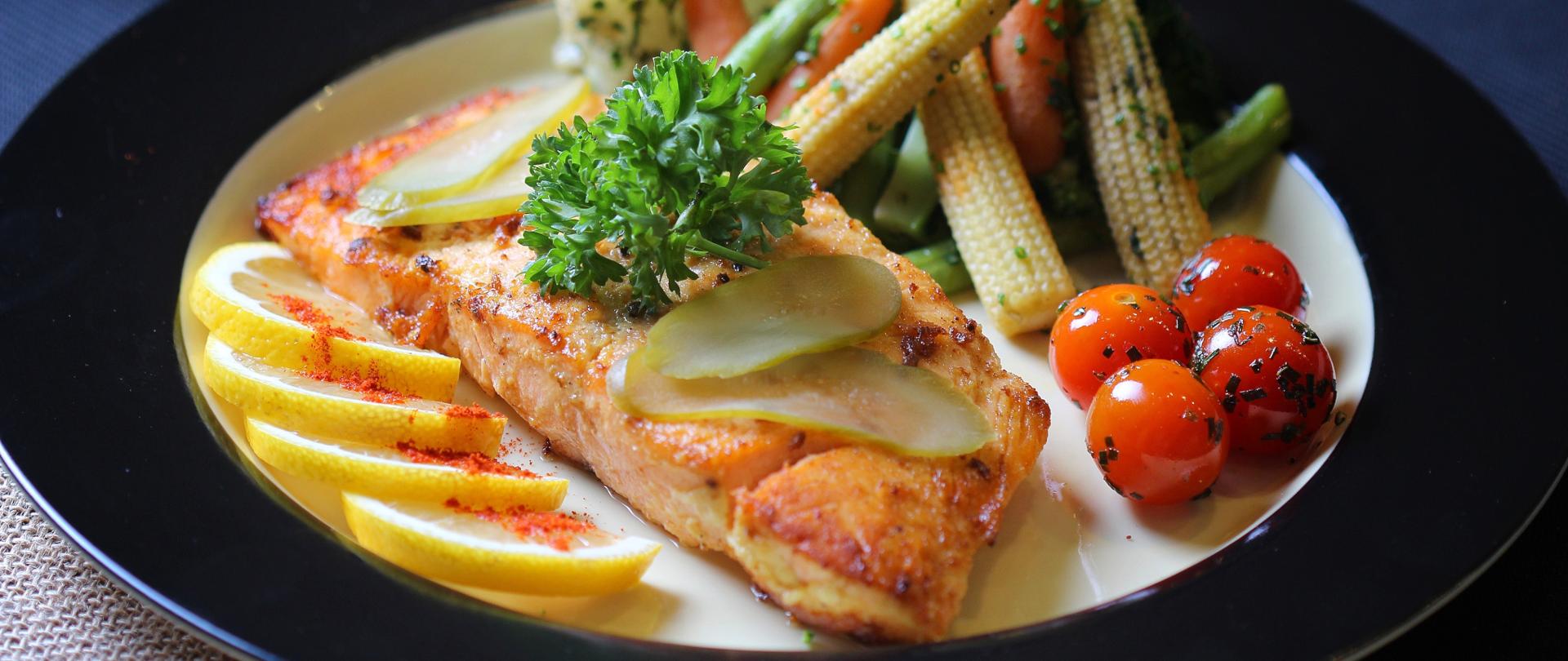 Upieczony filet z ryby ułożony na talerzy razem z warzywami.
