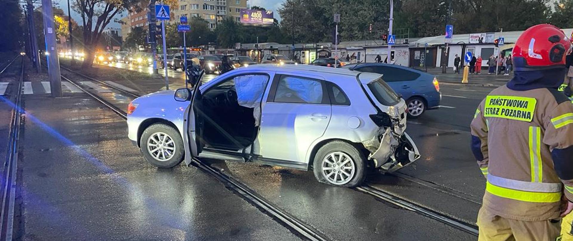  Na zdjęciu widać uszkodzony samochód biorący udział w zdarzeniu. Na zdjęciu widać również pracujących strażaków. 