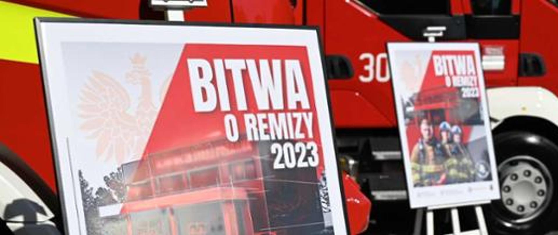 Banery akcji "Bitwa o remizy" na stelażach na tle czerwonych samochodów pożarniczych