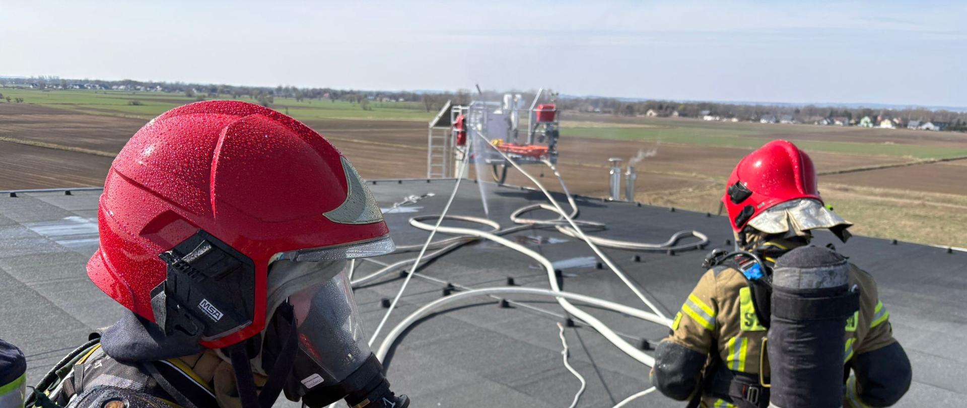 Na zdjęciu strażacy podczas ćwiczeń na dachu obiektu, w tle kosz podnośnika strażackiego