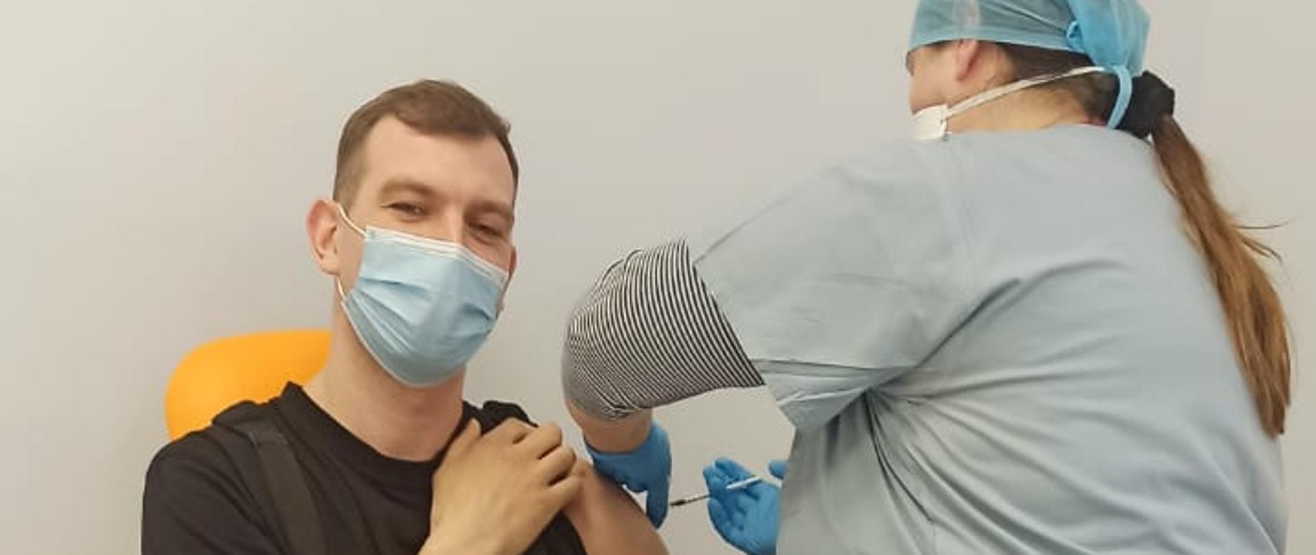 Zdjęcie przedstawia mężczyznę siedzącego na fotelu, który jest sczepiony przez pielęgniarkę.