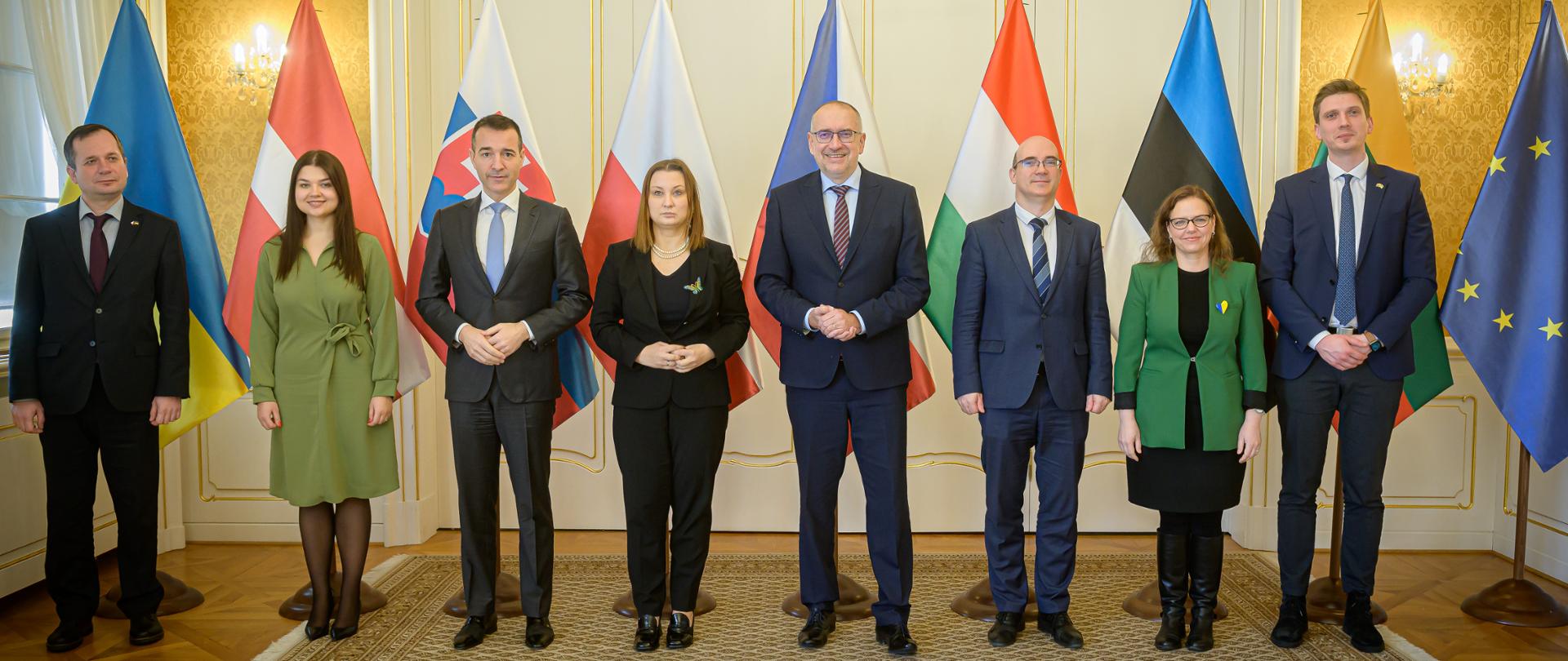 Osiem osób, kobiet i mężczyzn stoi i pozuje do zdjęcia. Za nimi flagi krajów z których pochodzą.