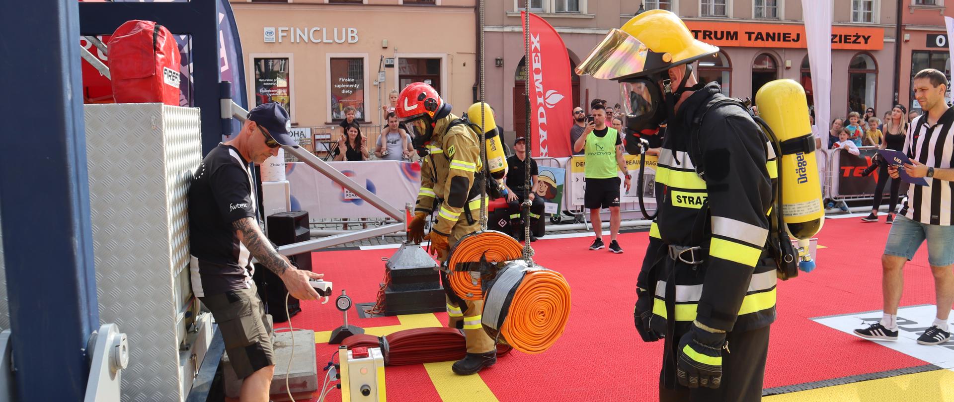 Widać zawodników na linii startu. Ubrani w mundury regulaminowe zawodów. W tle sceneria Rynku.