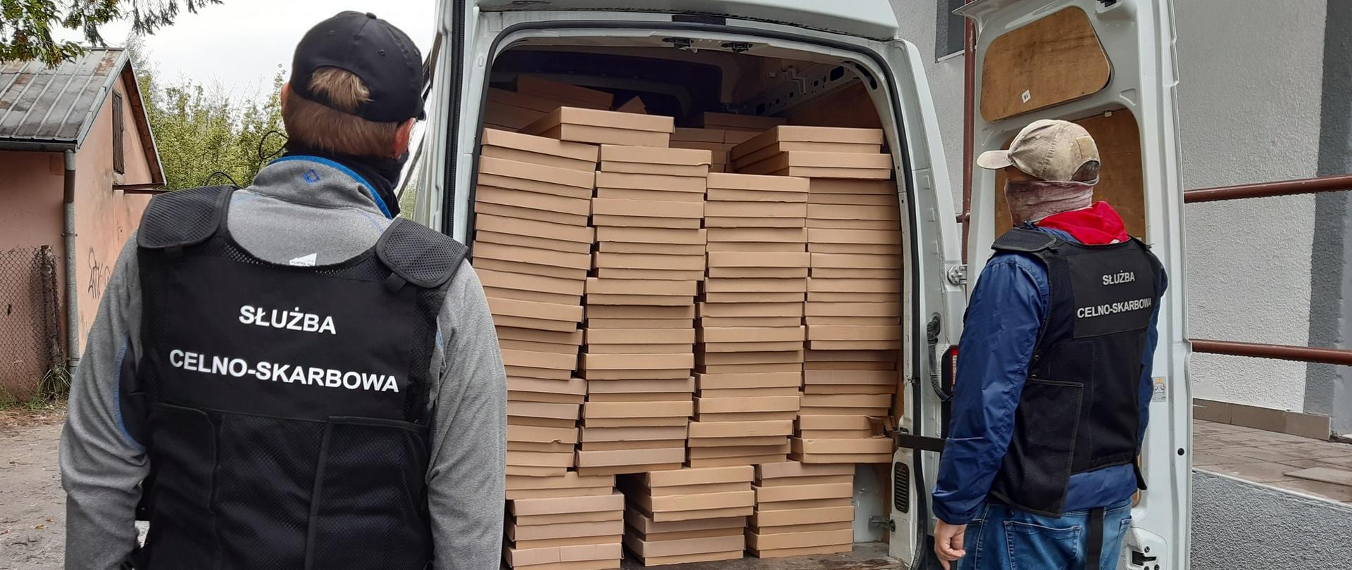 Dwóch funkcjonariuszy KAS przy samochodzie dostawczym. W środku kartony z nielegalnymi papierosami 