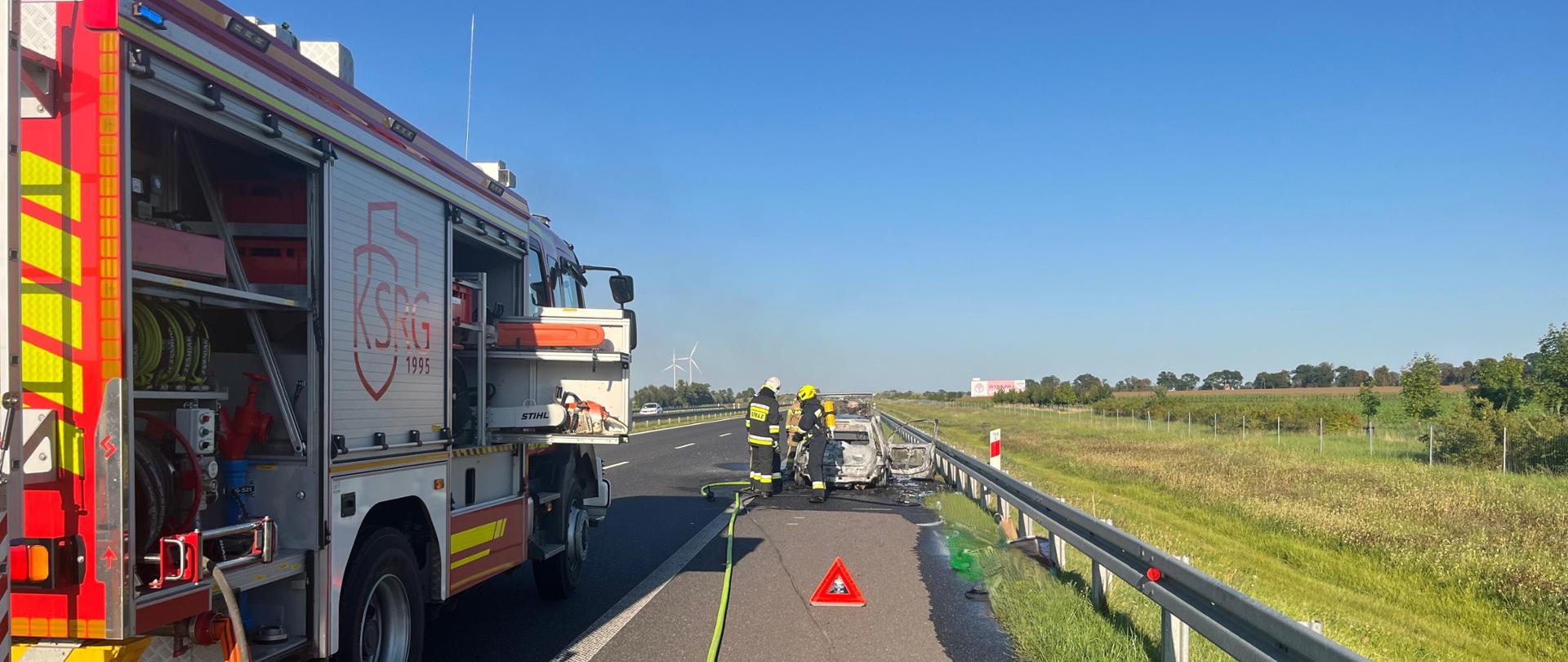 Samochód osobowy po pożarze oraz strażacy
