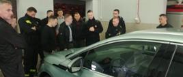 Zdjęcie przedstawia samochód elektryczny oraz strażaków Państwowej Straży Pożarnej podczas szkolenia z pojazdów elektrycznych