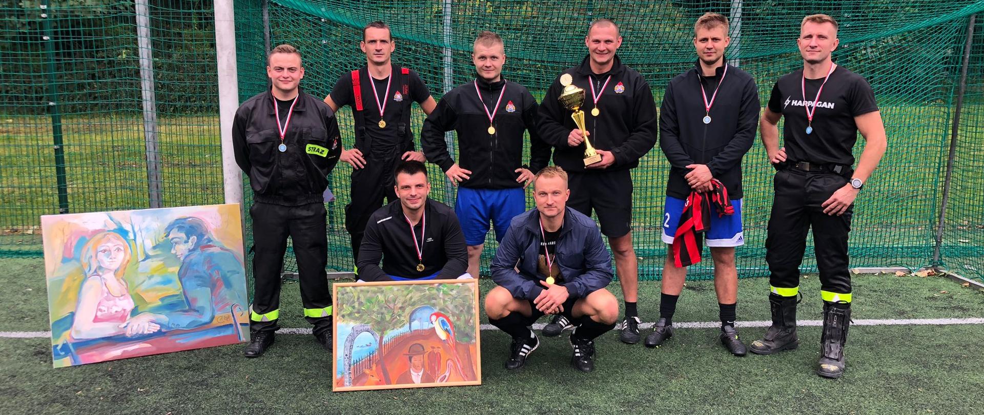 Zdjęcie przedstawia drużynę piłkarską Komendy Miejskiej Państwowej Straży Pożarnej w Chorzowie po zakończonym turnieju na tle bramki 