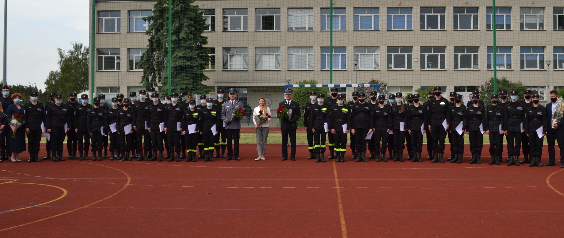 Zdjęcie grupowe awansowanych i nagrodzonych uczniów klas mundurowych wraz z Komendantami Powiatowymi PSP i Policji oraz Dyrektor Szkoły