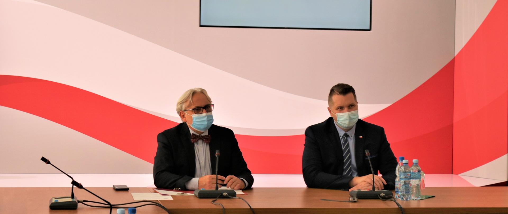 Minister i wiceminister siedzą za stołem w maseczkach.