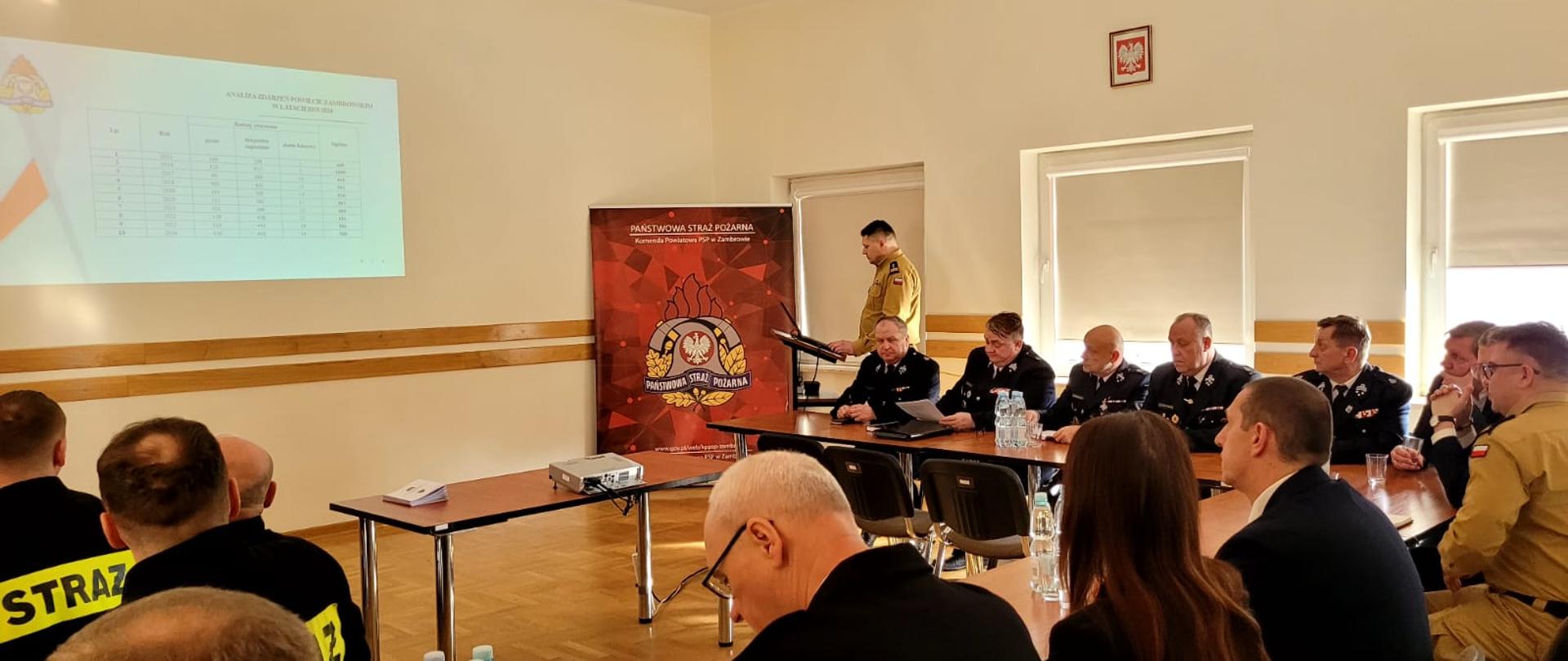 Narada roczna podsumowująca funkcjonowanie ochrony przeciwpożarowej na terenie powiatu zambrowskiego za rok 2024. Przemówienie komendanta powiatowego i prezentowanie treści na sali.