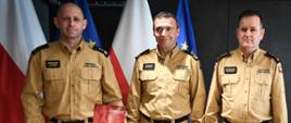 Zdjęcie zrobione wewnątrz pomieszczenia. Na zdjęciu stoi trzech oficerów Państwowej Straży Pożarnej.