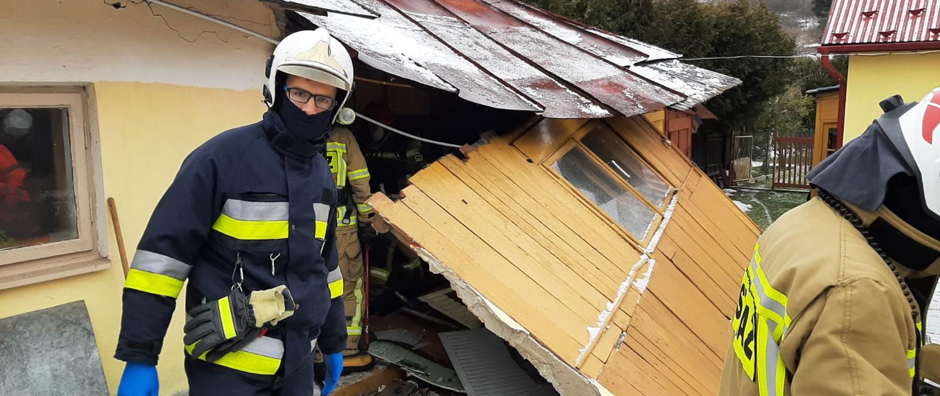 Strażacy przed zniszczonym po wy buchu budynkiem. Widać pochyloną ścianę.