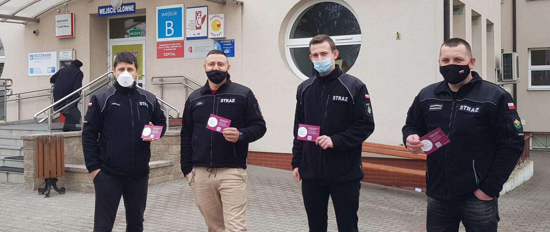 czterech strażaków stoi przed budynkiem szpitala