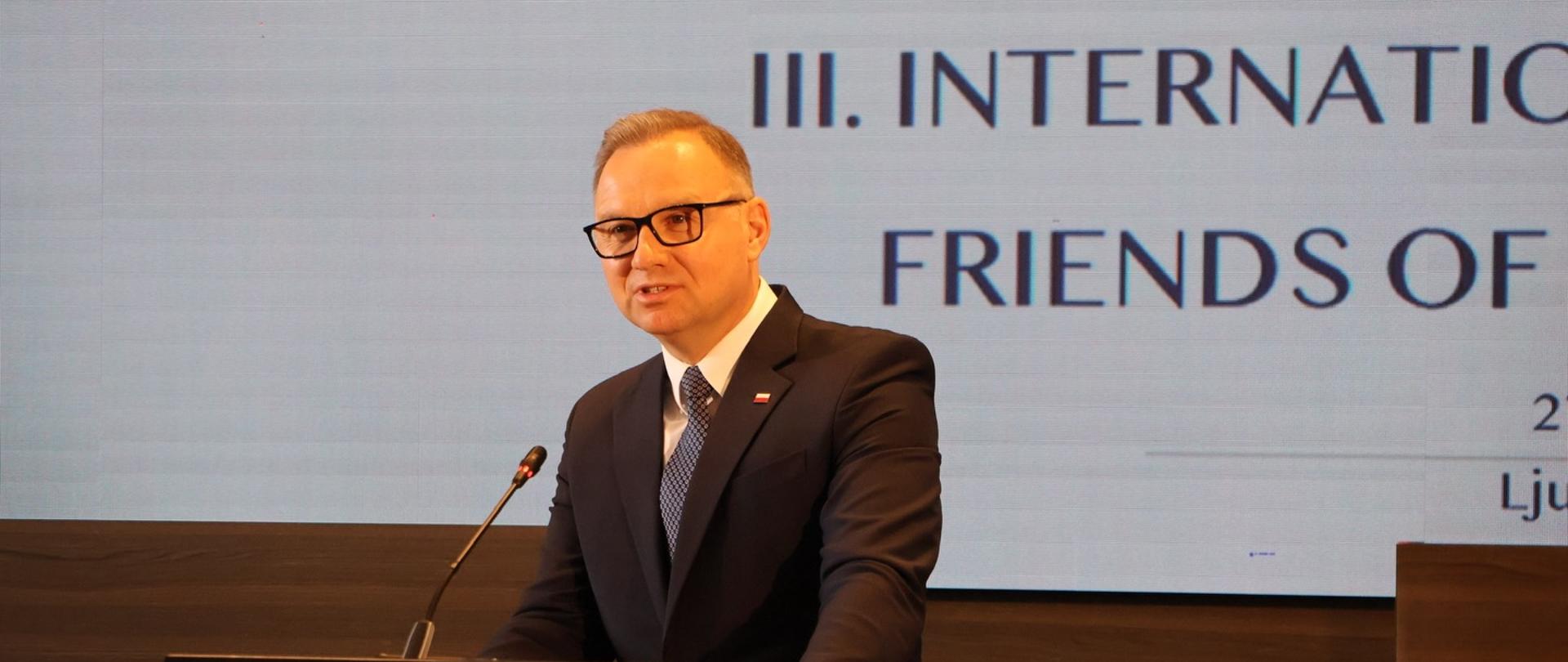 Moški v obleki govori za govorniškim pultom na konferenci. V ozadju je zaslon z napisom o konferenci »Friends of the Western Balkans«.