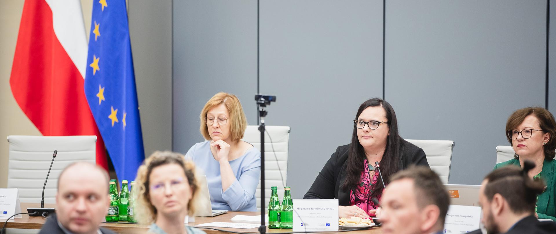 Trzy osoby siedzą obok siebie przy stole. W środku jest wiceminister Małgorzata Jarosińska-Jedynak.