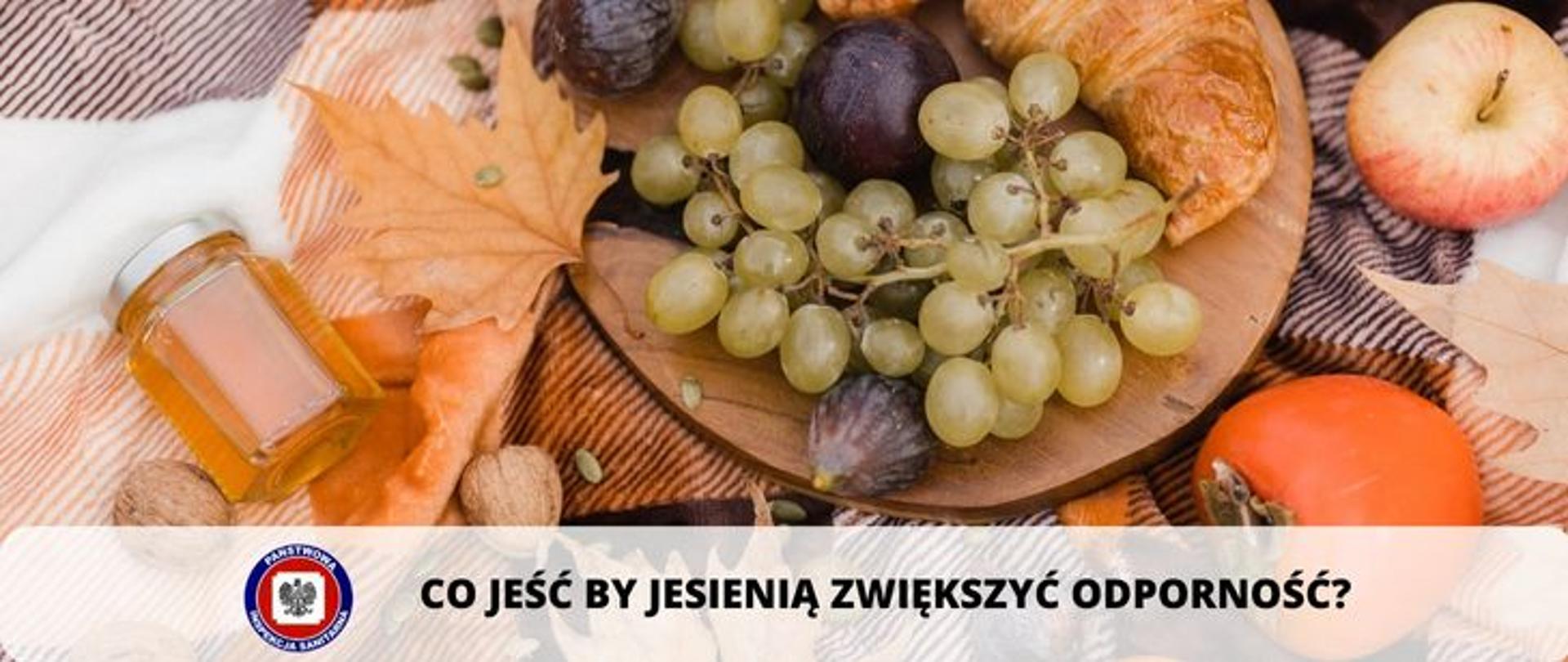 Zdjęcie przedstawia deskę z owocami rogalikiem , obok słoiczek z miodem