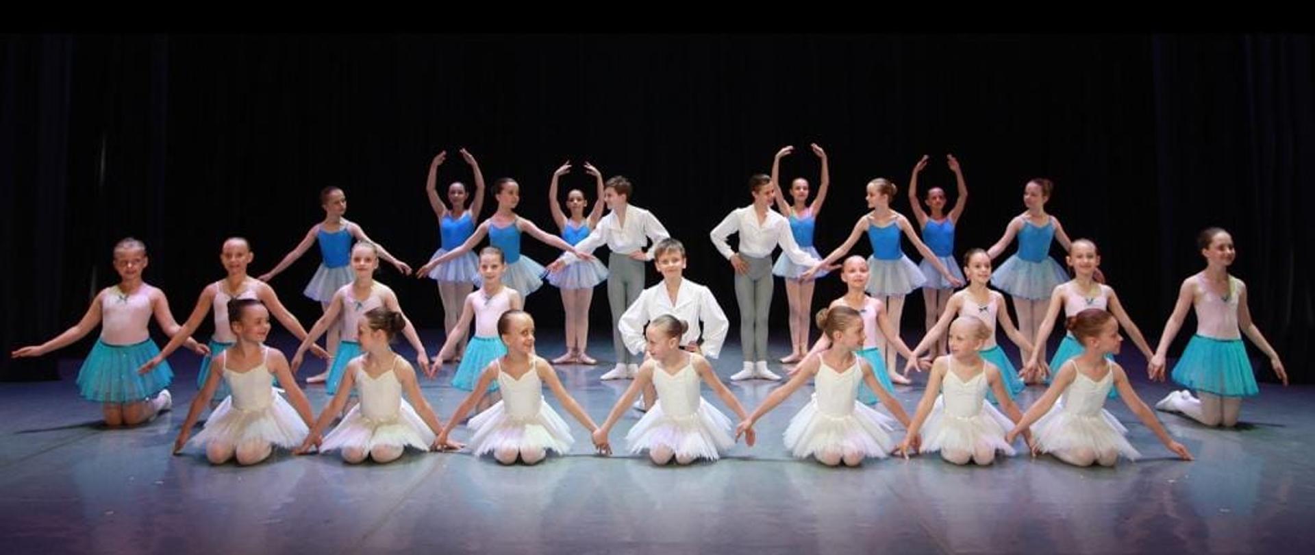 Na zdjęciu grupa dzieci w pozach baletowych. Dzieci znajdują się na scenie.