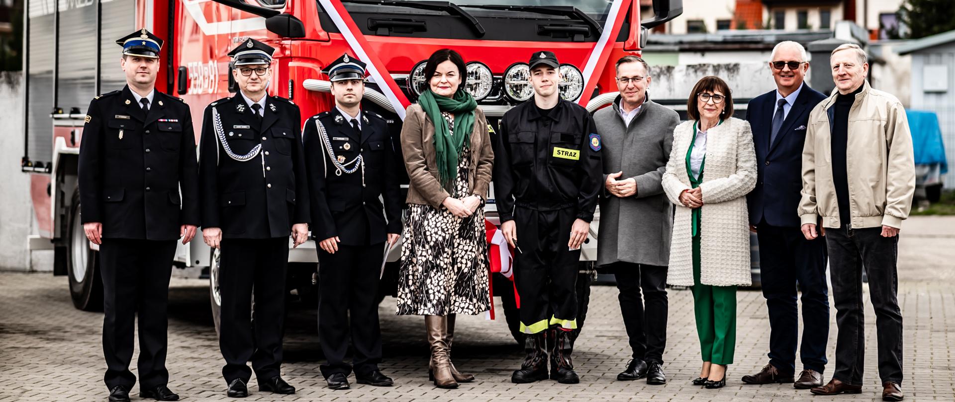 Wspólne zdjęcie strażaków OSP i gości przed samochodem.
