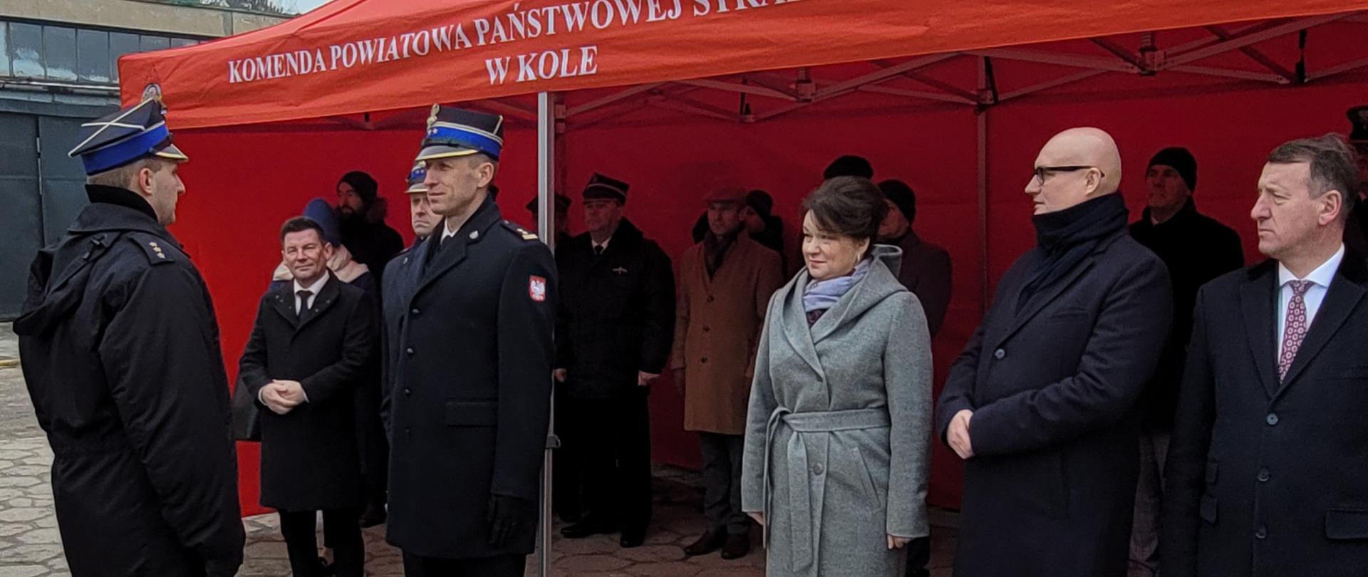 składanie meldunku przez strażaka drugiemu strażakowi, w tle czerwony namiot z grupą ludzi