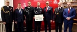 Zdjęcie przedstawia strażaków OSP z jednostki w Dukli w towarzystwie Posła na Sejm PR Piotra Babineza, Prezesa Zarządu Wojewódzkiego Funduszu Ochrony Środowiska i Gospodarki Wodnej w Rzeszowie Adama Skiby, Zastępcy Burmistrza Gminy Dukla Łukasza Piroga oraz Zastępcy Podkarpackiego Komendanta Wojewódzkiego st. bryg. Daniela Dryniaka i Komendanta Miejskiego PSP 