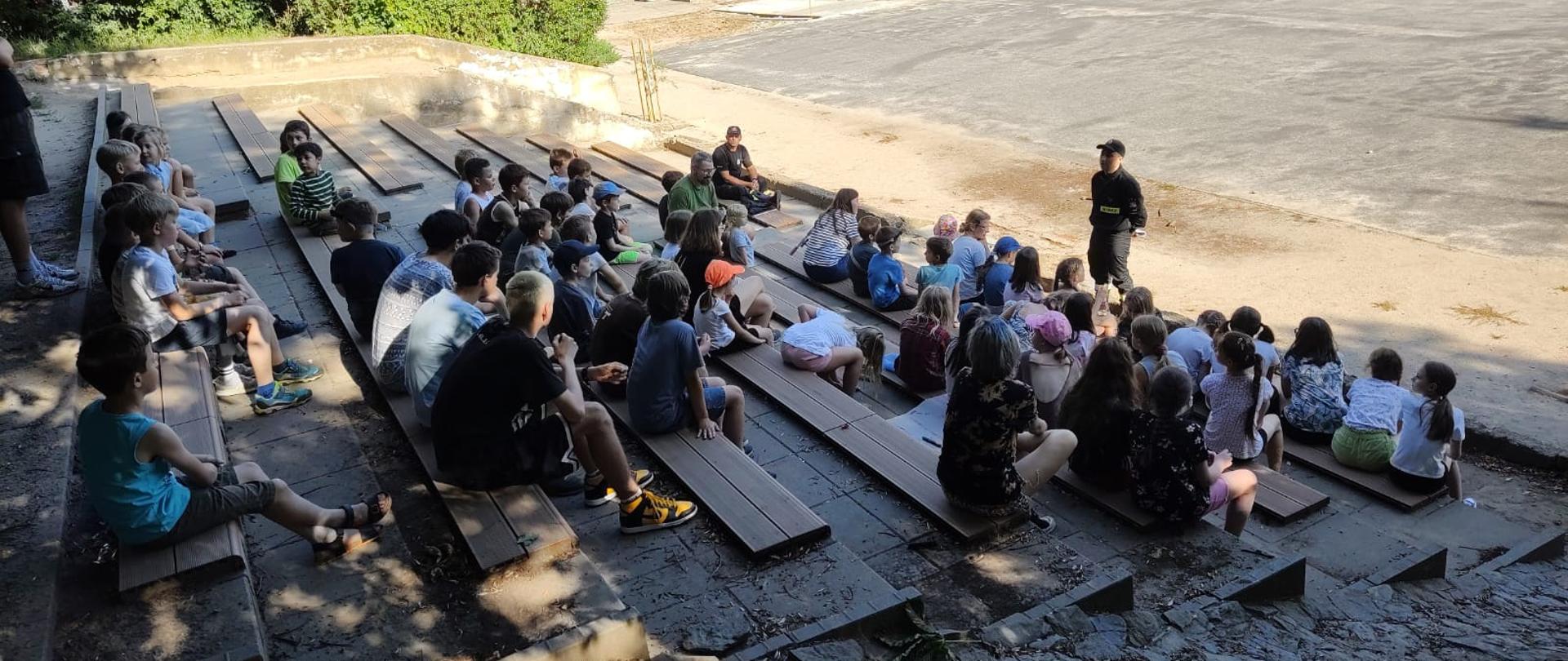 Na zdjęciu strażak przed grupą dzieci biorących udział w turnusie obozowym
