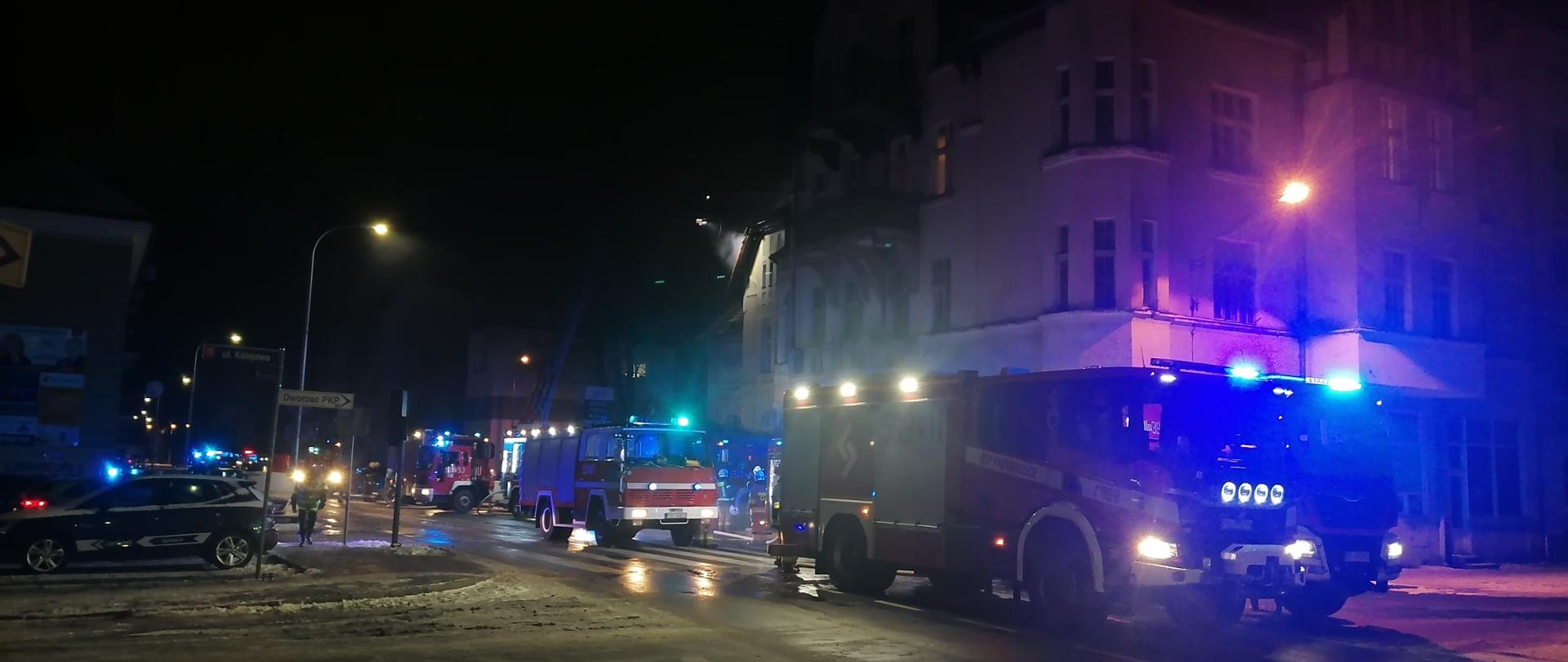 Samochody pożarnicze ustawione jeden za drugim ze światłami błyskowymi w nocy.