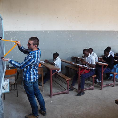 mężczyzna stoi przy tablicy, uczniowie notują 