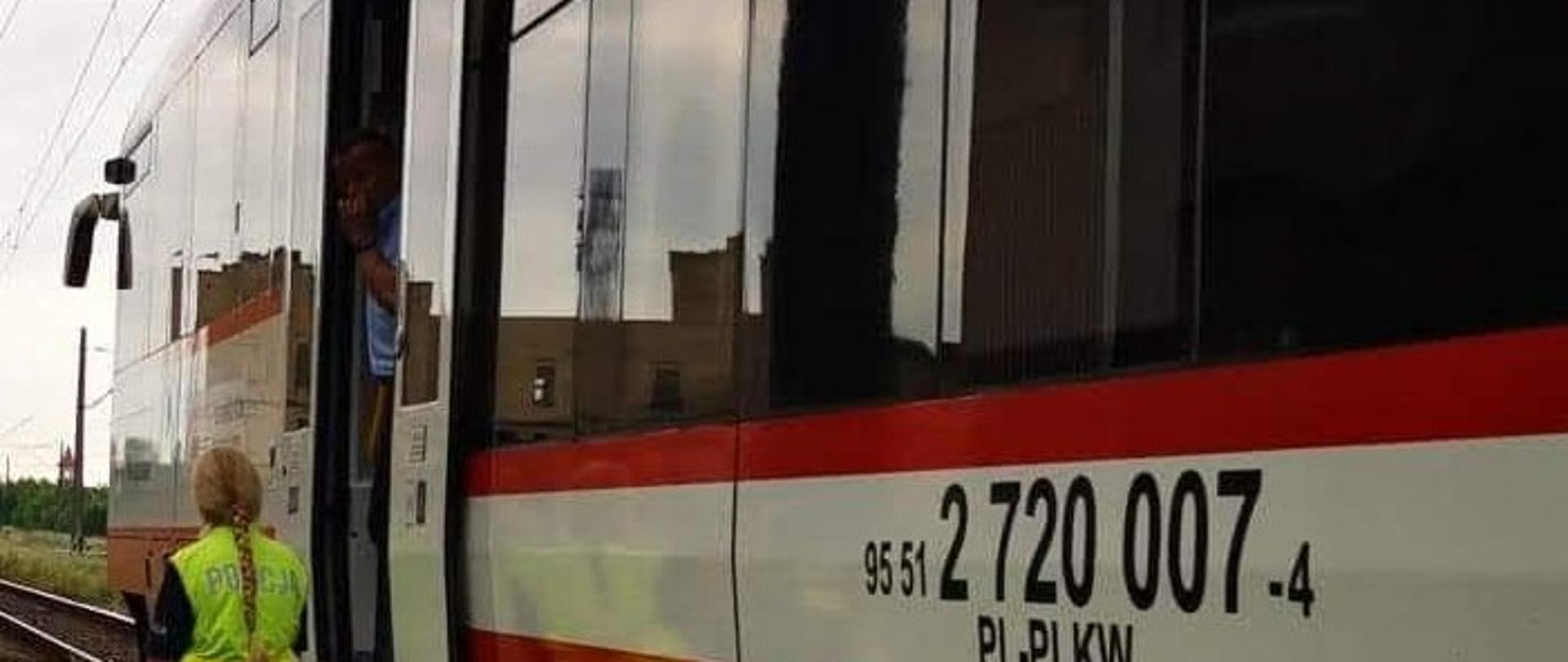 Zdjęcie przedstawia szynobus oraz fragment torów. Obok szynobusu stoi funkcjonariusz Policji. W górze widoczna trakcja kolejowa