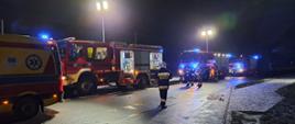 Zdjęcie wykonane w porze nocnej. Widać pojazdy ratowniczo-gaśnicze z sygnalizacją ostrzegawczą. Zdjęcie wykonane na drodze publicznej. Oświetlenie sztuczne. Widać ratowników.
