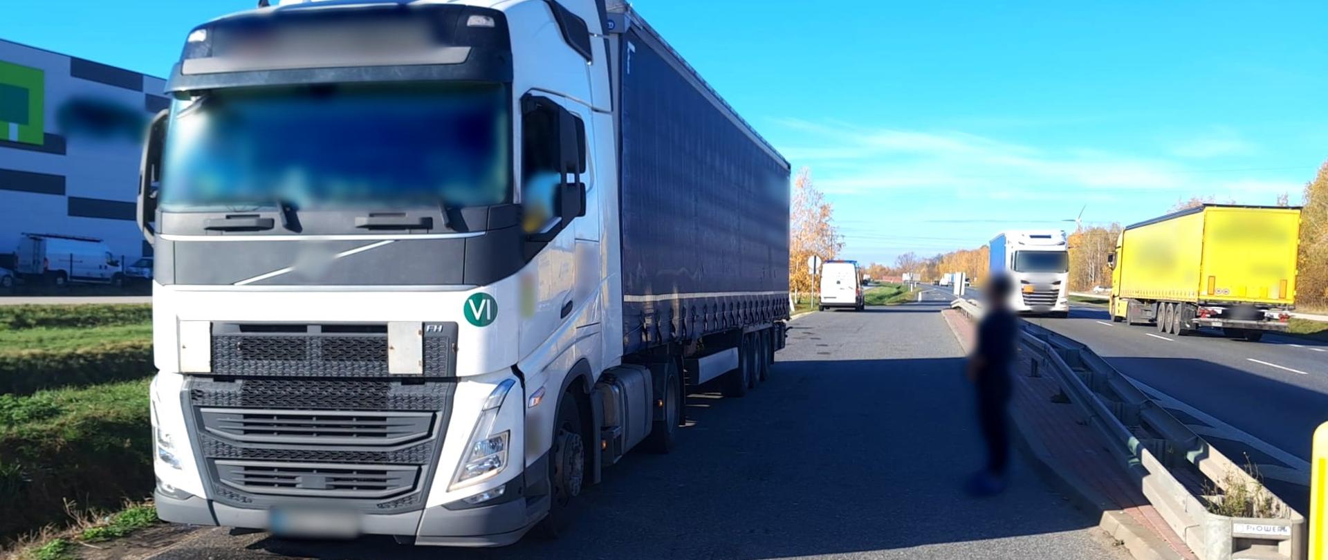 Na pierwszym planie (od lewej): ciągnik siodłowy z podpiętą naczepą kurtynową. Obok zestawu ciężarowego stoi kierowca. W tle: tył oznakowanego furgonu mazowieckiej Inspekcji Transportu Drogowego.