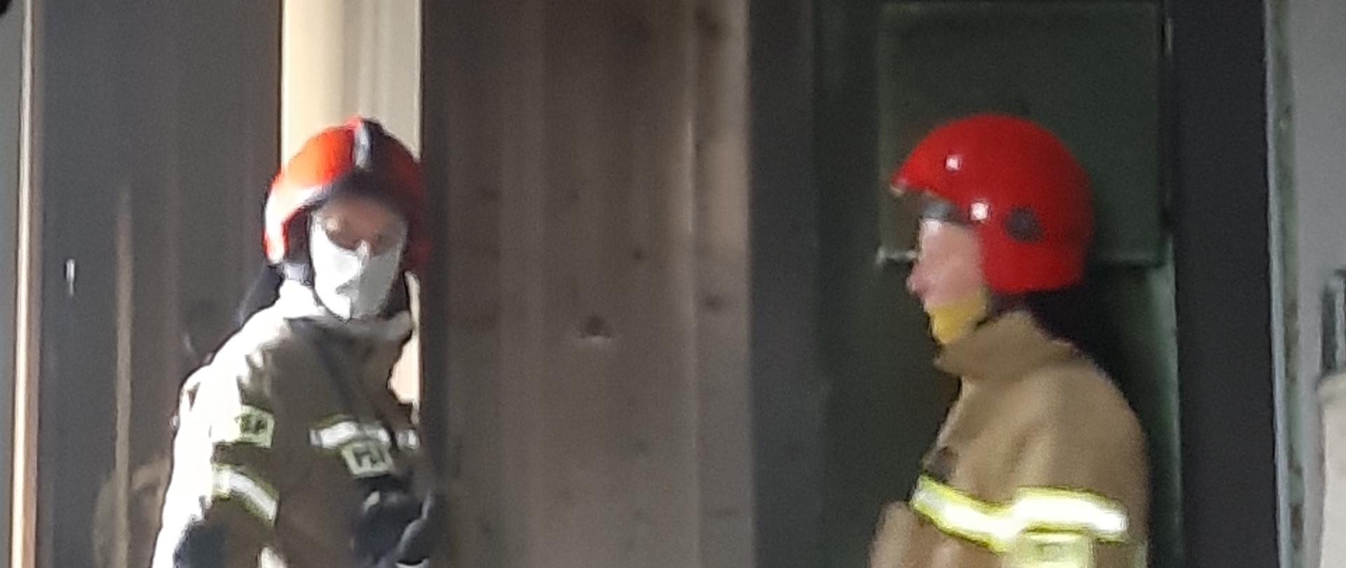 Na zdjęciu widoczna jest część klatki schodowej w budynku, w którym doszło do pożaru. W dolnej części znajdują się dwaj strażacy z jednostki ratowniczo-gaśniczej w Chrzanowie w umundurowaniu specjalnym. W górnej części zdjęcia widoczne są szkody spowodowane pożarem.