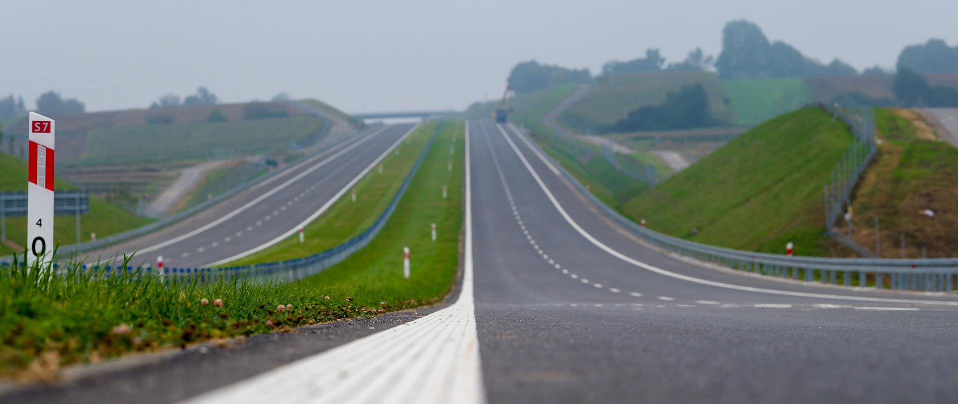 Droga ekspresowa S7 na odcinku Szczepanowice - Widoma tuż przed oddaniem do ruchu. Dwujezdniowa droga ekspresowa, po dwa pasy ruchu w obu kierunkach. Zdjęcie wykonane blisko gruntu. Widoczny biały pas oznakowania oddzielający pas ruchu od krawędzi drogi. Po lewej biały słupek pikietażowy z nr drogi ekspresowej.