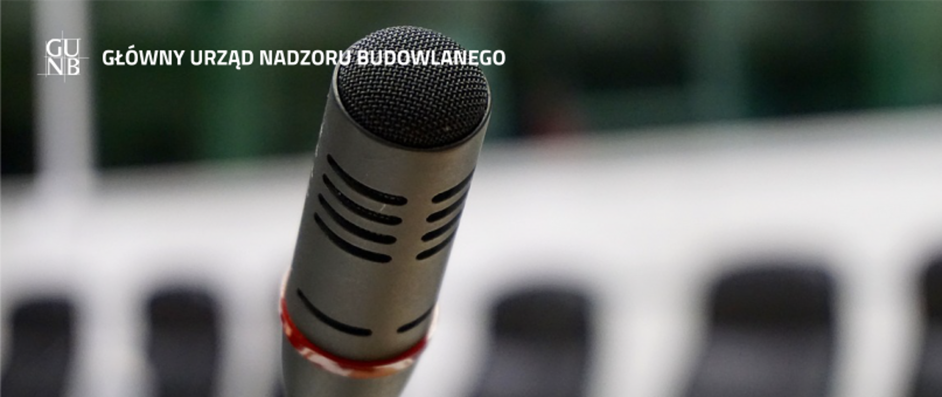 „Zbliżenie na mikrofon, w tle napis 'Główny Urząd Nadzoru Budowlanego' i logo GUNB.”