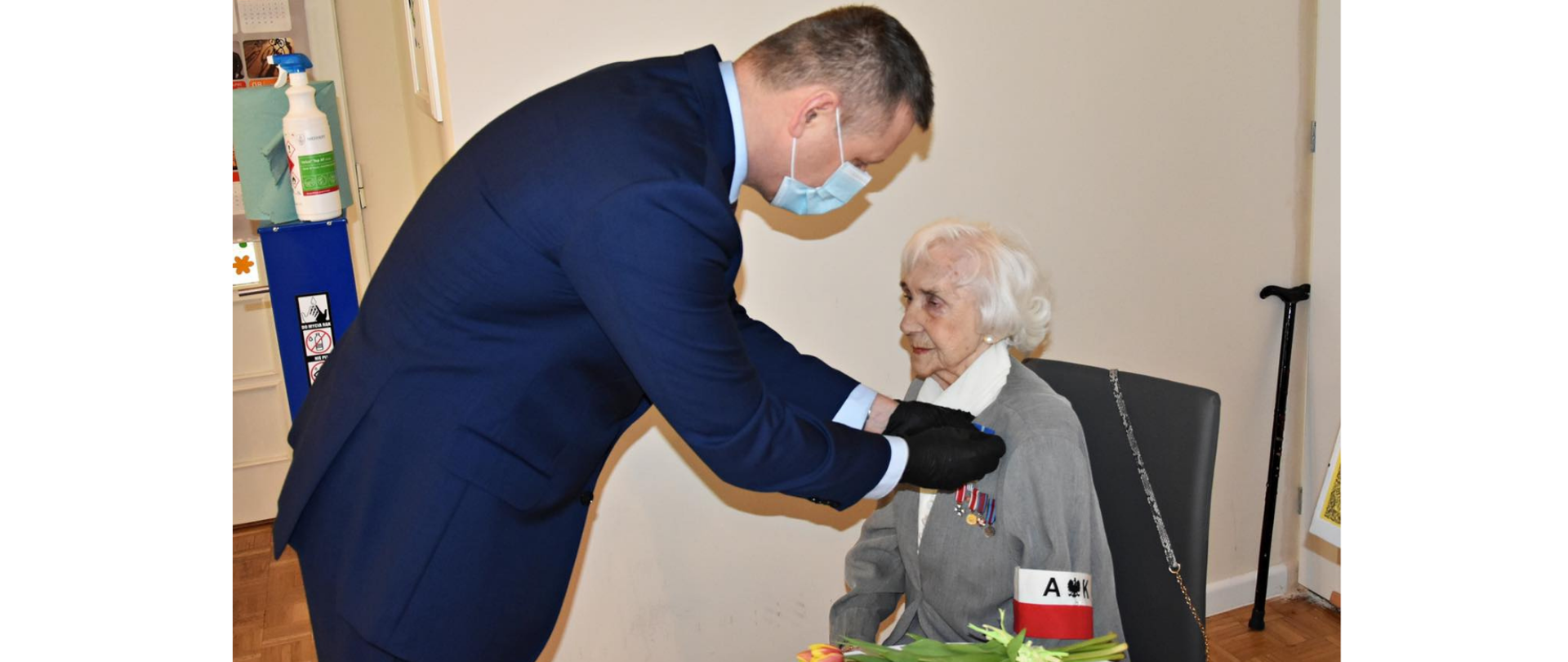Na zdjęciu znajduje się mężczyzna, który przypina medal starszej kobiecie. 