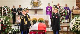 Przy trumnie odzianej w Polską flagę wartę pełnią generałowie straży pożarnej. Przed trumną na poduszkach są medale. Dookoła wieńce pogrzebowe. 
