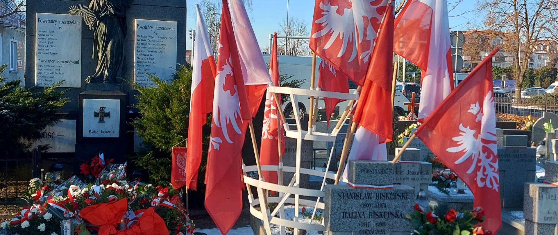 Flagi na stojaku stoją obok nagrobków.