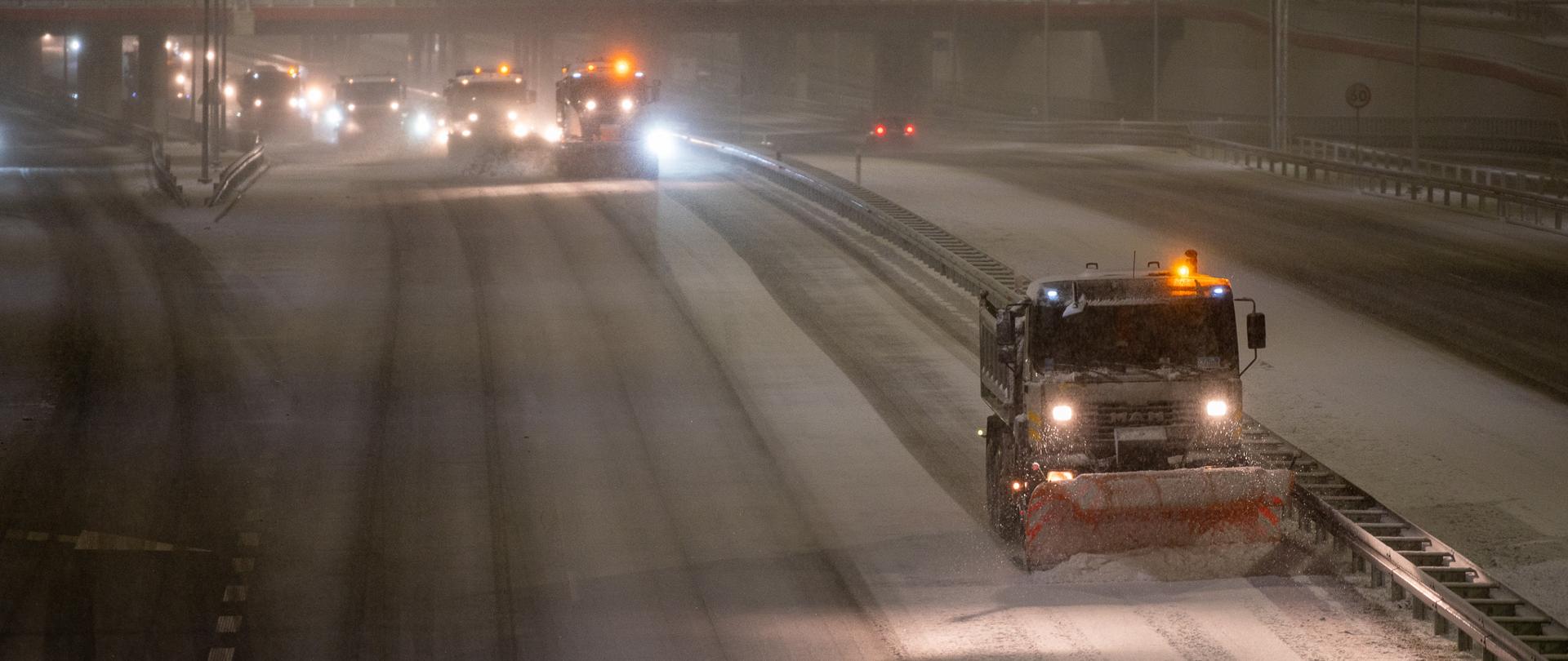 Jest ciemno. Widoczne pługi odśnieżające drogę ekspresową.