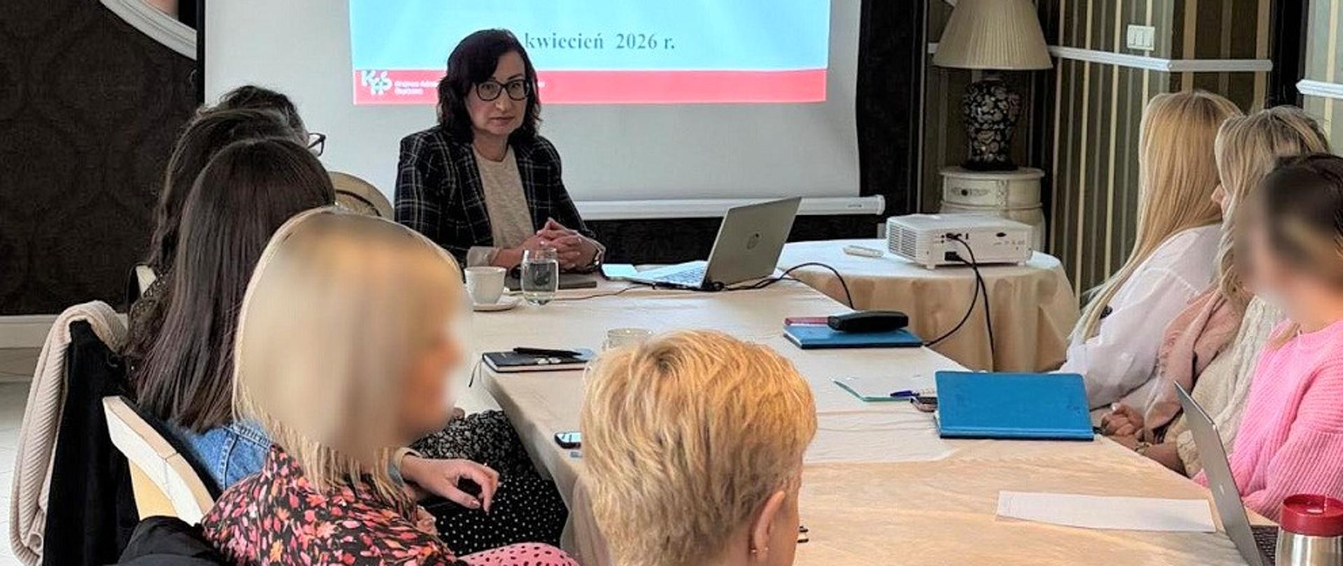 Ekspertka i uczestnicy szkolenia siedzą w sali. Na ekranie wyświetlana jest prezentacja.