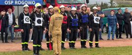 Drużyna męska z Rogowa ustawiona w dwuszeregu, przed rozpoczęciem ćwiczenia składa meldunek o gotowości do przeprowadzenia ćwiczenia bojowego.
