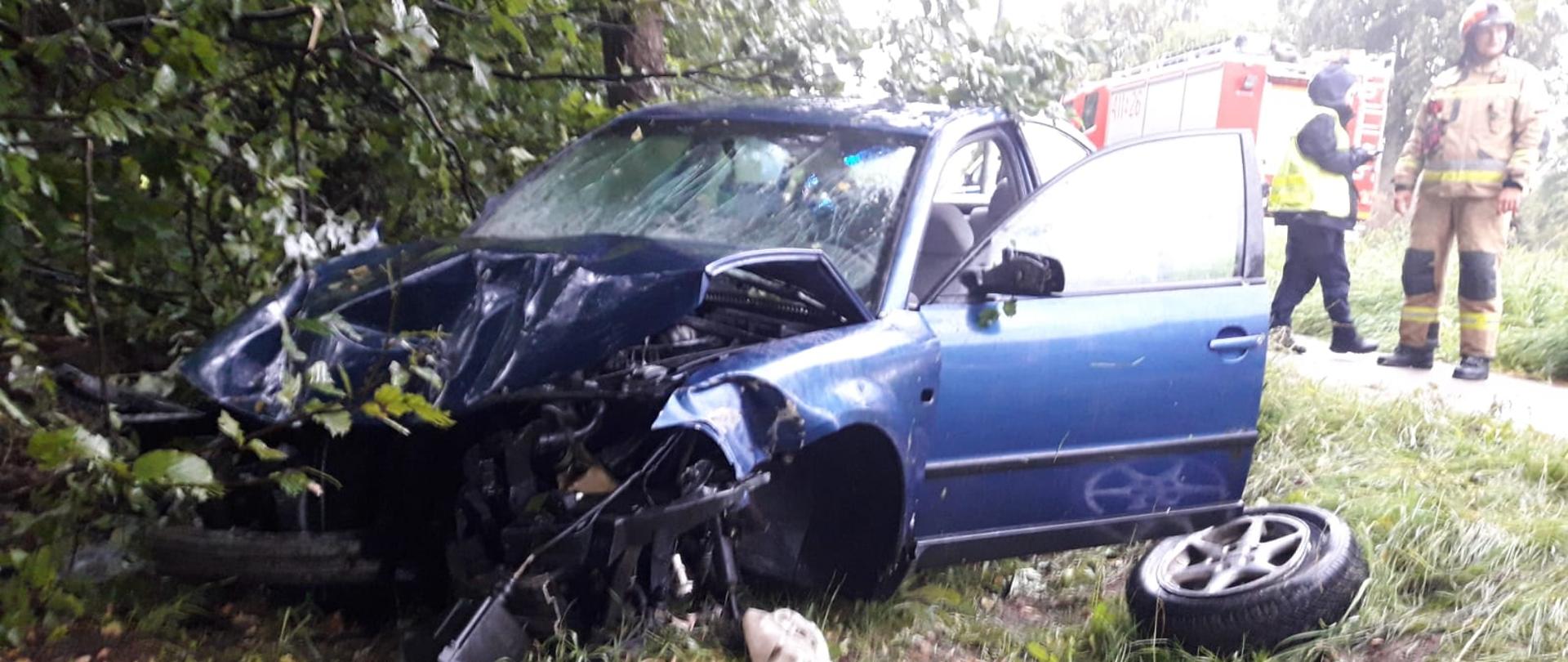 Rozbity niebieski samochód poza drogą. N drodze służby ratownicze.