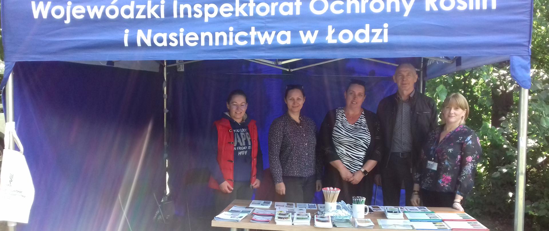 Pracownicy Oddziału w Wieluniu pozujący do zdjęcia pod niebieskim namiotem. W pierwszym planie stolik na którym leża kolorowe ulotki.