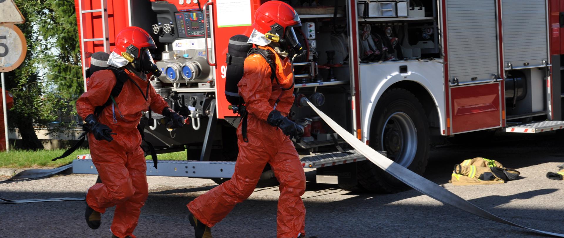 Strażacy w pomarańczowych ubraniach ochronnych udają się na rozpoznanie miejsca zdarzenia