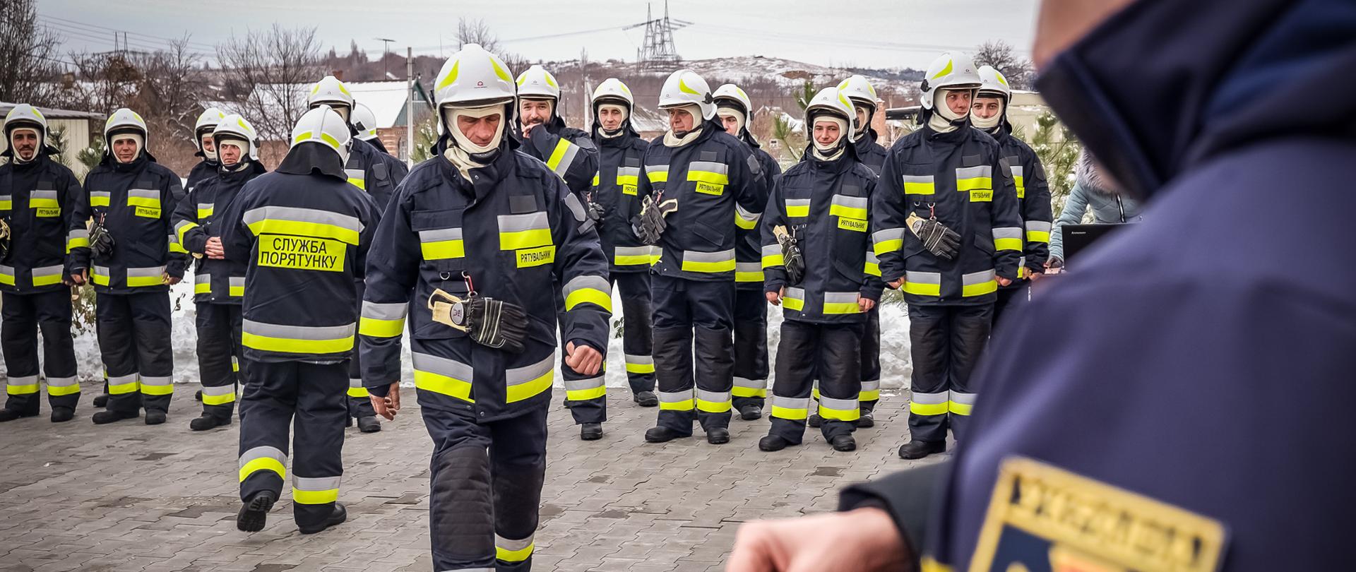 z grupy strażaków, wychodzi jeden i zmienia w kierunku obiektywu