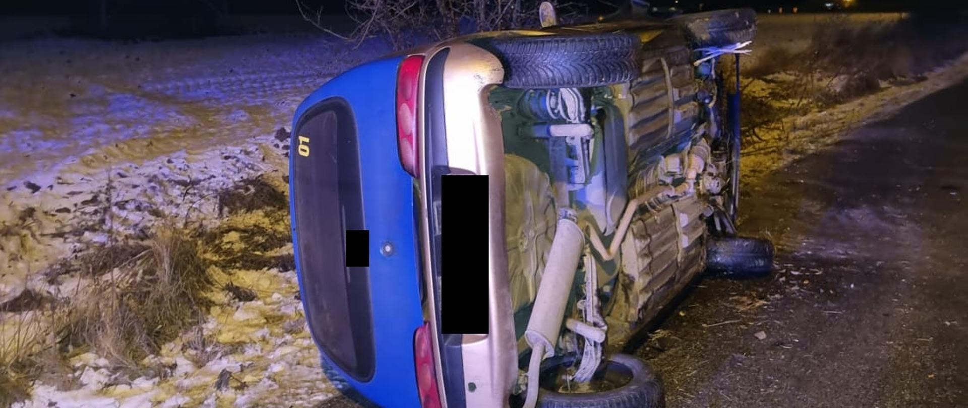 Widać samochód os tyłu, który jest na lewym boku na drodze, jest ciemno