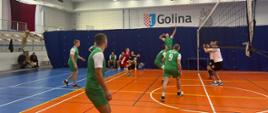 Zdjęcie przedstawia strażaków grających w piłkę siatkową na hali sportowej. 