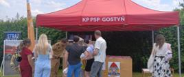 Stoisko Państwowej Straży Pożarnej na Eko-Festynie.
Pod czerwonym namiotem z napisem KP PSP Gostyń, znajduje się mobilny symulator zagrożeń pożarowych. Strażak pokazuje przybyłym osobom jak działa taki symulator. Z lewej strony znajduje się ścianka do zdjęć.